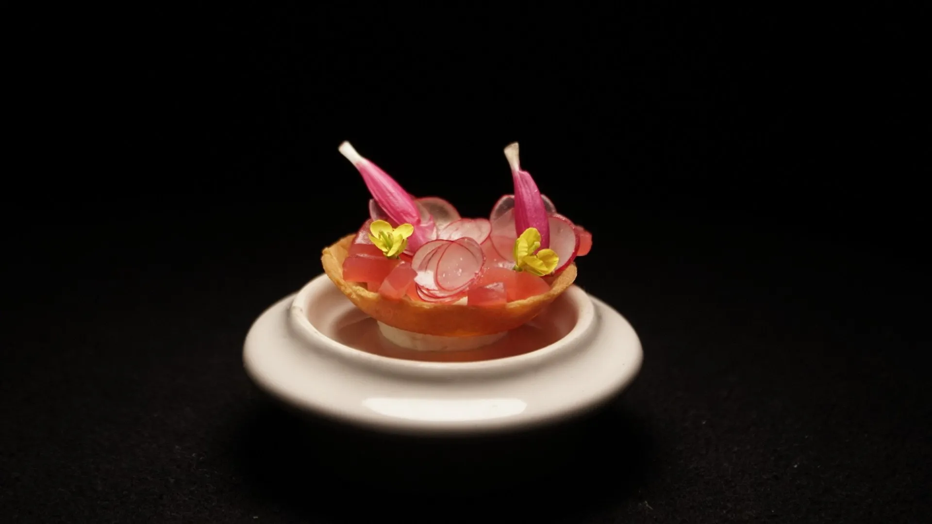 Elegant gourmet appetizer garnished with pink flowers and greens on a small white dish