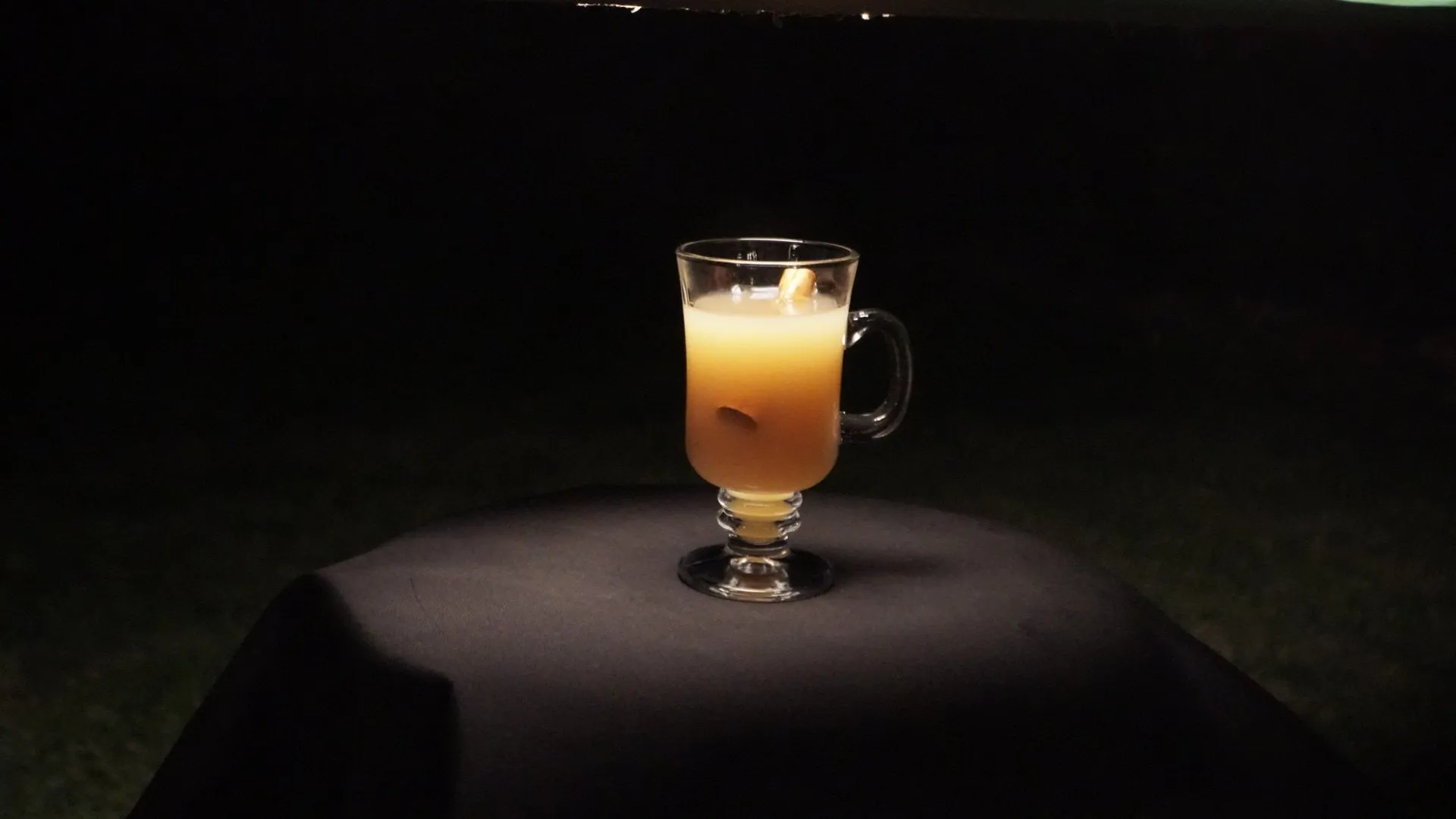 Glass mug filled with an orange beverage placed on a dark table under focused lighting