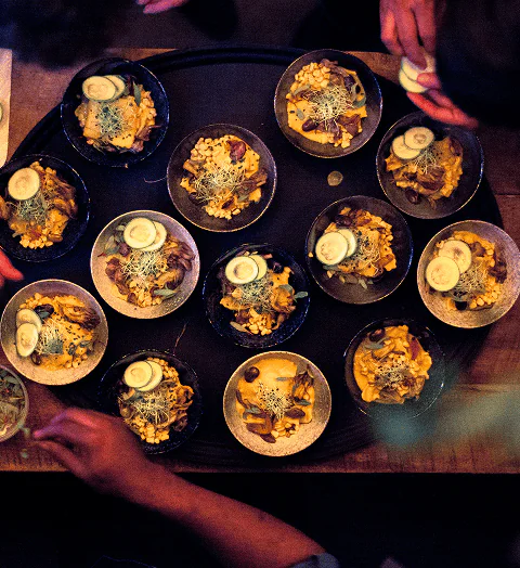 Top view of multiple bowls of food with hands reaching for them on a serving tray